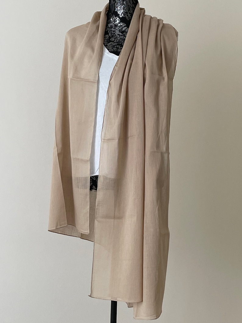 May include: A light brown sheer scarf draped over a mannequin. The scarf is made of a lightweight fabric and has a simple, elegant design.