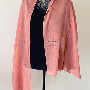 May include: A coral peach colored scarf made of a lightweight fabric. The scarf is draped over a black mannequin.