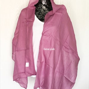 May include: A soft, sheer, onion pink scarf draped over a white shirt on a mannequin. The scarf is made of a lightweight fabric and has a delicate drape.