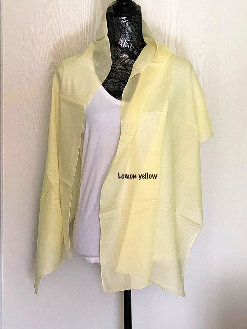 May include: A lemon yellow sheer scarf draped over a white mannequin. The scarf is made of a lightweight fabric and has a simple design.