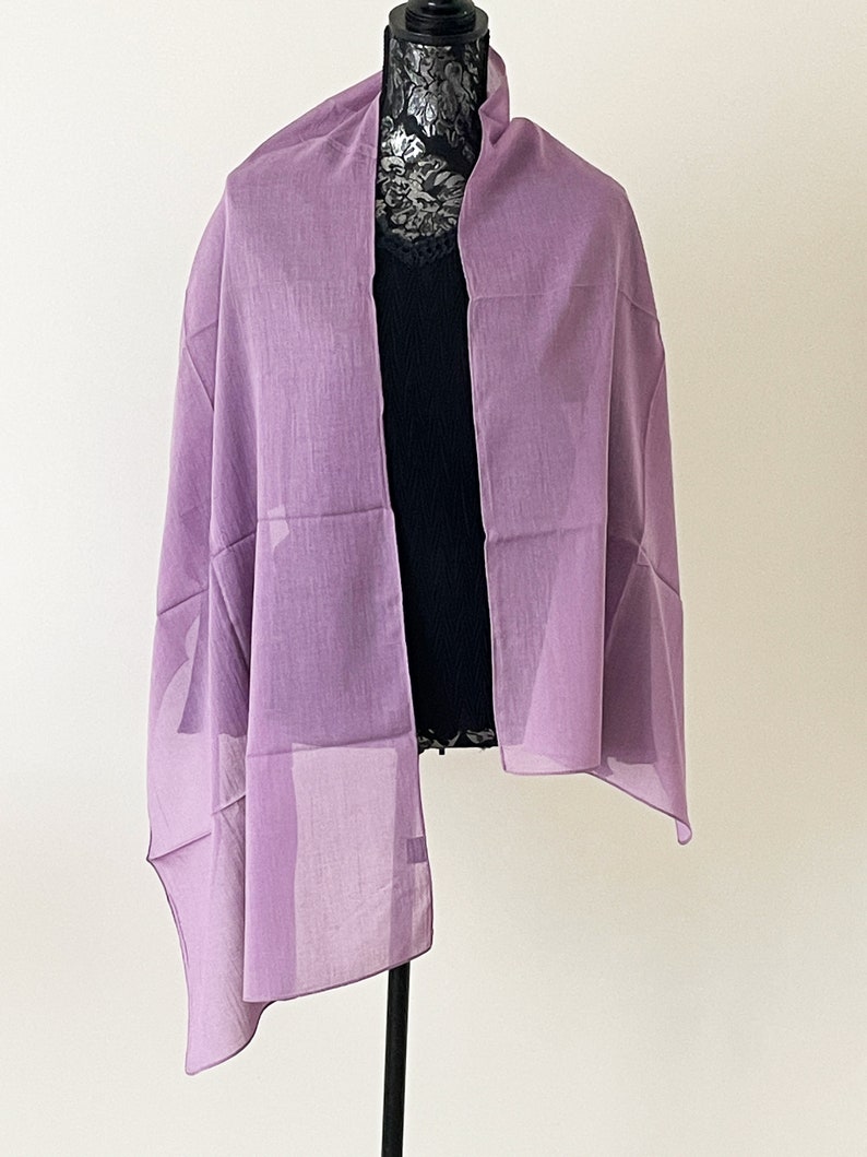 May include: A light purple sheer scarf draped over a mannequin. The scarf is made of a lightweight fabric and has a simple, elegant design.
