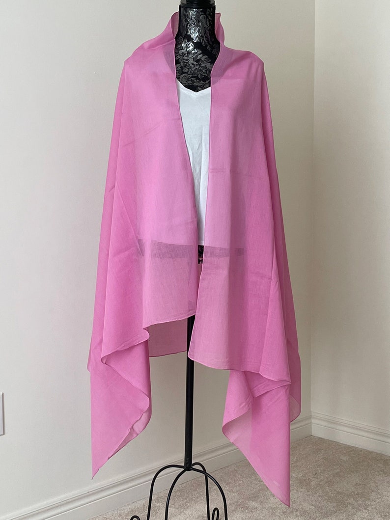 May include: A pink cotton scarf draped over a mannequin. The scarf is lightweight and sheer, with a soft, drapey texture.