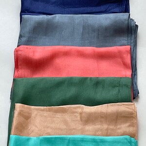 May include: Six different colored fabric squares stacked on top of each other. The colors are navy blue, gray, coral, forest green, beige, and teal.