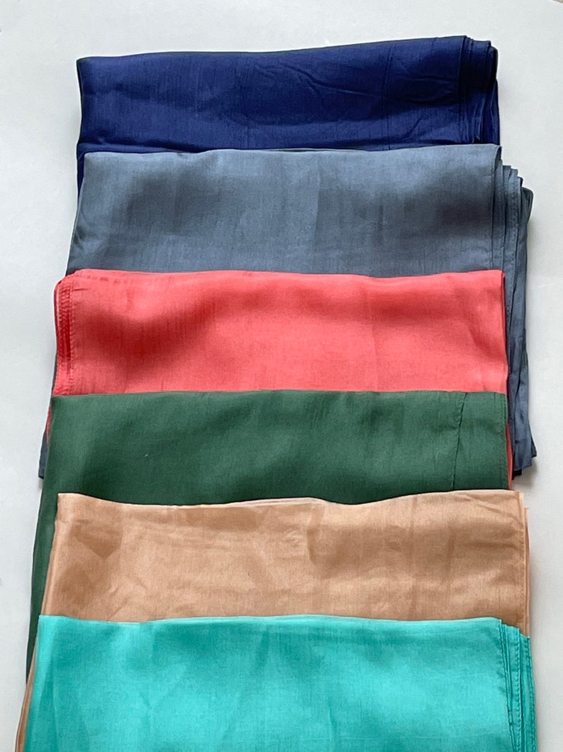 May include: Six different colored fabric squares stacked on top of each other. The colors are navy blue, gray, coral, forest green, beige, and teal.