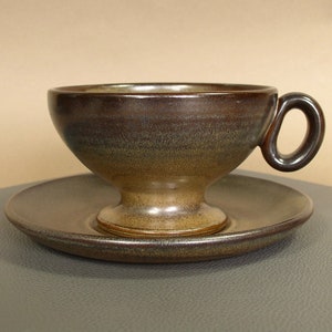 May include: A brown ceramic teacup and saucer set with a flared, footed cup and a rounded saucer.