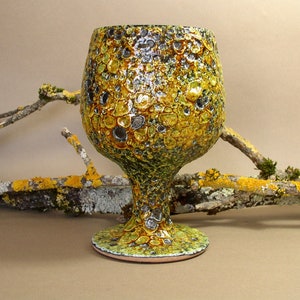 May include: A yellow and green ceramic goblet with a textured surface. The goblet has a round bowl and a tall stem.