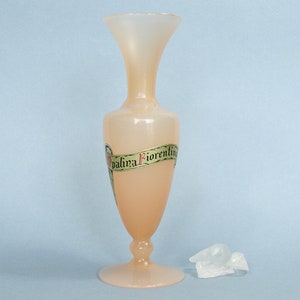 Op de afbeelding: Een lichtroze glazen vaas met een gouden en groen lint om het midden. Het lint heeft de tekst "Palina Fiorentine" erop.