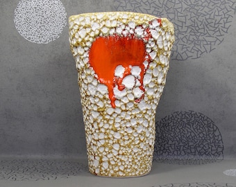 May include: A white ceramic vase with a textured surface and a large orange drip glaze. The vase is tall and narrow with a rounded base.