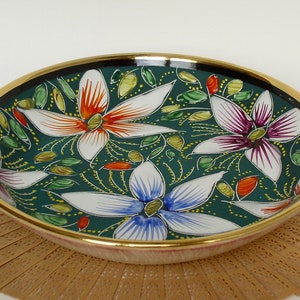 May include: A green ceramic bowl with a gold rim and a floral design. The bowl features white, red, orange, purple, and blue flowers on a green background.