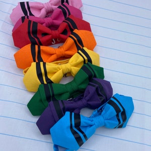 Può includere: Un set di sette papillon in colori arcobaleno con strisce nere. I papillon sono disposti in una pila dal rosa al blu.