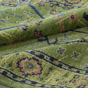 May include: A green rug with a traditional Persian design. The rug has a dark blue border and intricate floral patterns in shades of pink and blue.