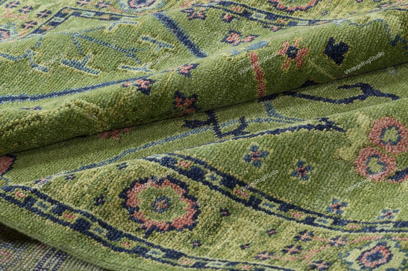 May include: A green rug with a traditional Persian design. The rug has a dark blue border and intricate floral patterns in shades of pink and blue.