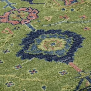 May include: Close-up of a green rug with a blue and pink floral pattern. The rug has a traditional design with intricate details.