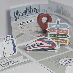 Könnte beinhalten: Eine Pop-up-Grußkarte mit Reisethema. Sie zeigt eine Karte, eine rote Stecknadel und Schilder, die auf „unvergessliche Erlebnisse“ hinweisen. Enthält einen Zug, einen Koffer, eine Kamera und den Text „Happy Birthday“.
