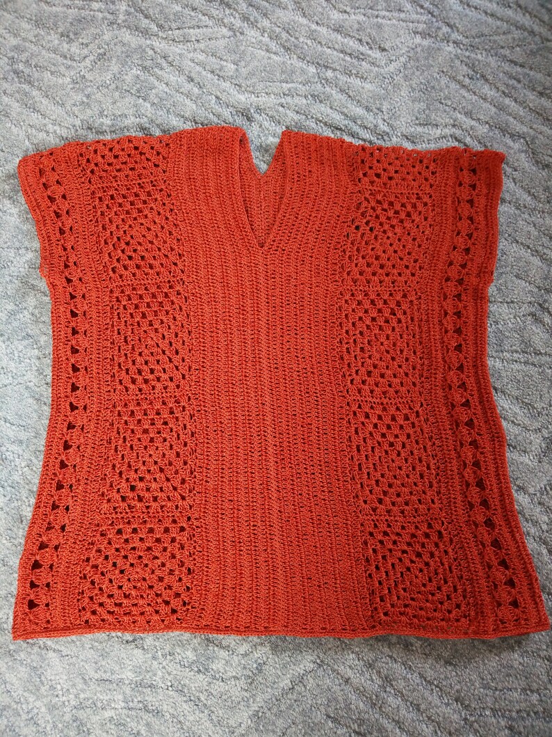 Może przedstawiać: Kr&oacute;tki sweterek wykonany na szydełku z dekoltem w kształcie litery V i bez rękaw&oacute;w. Sweterek jest wykonany z jasno pomarańczowej przędzy i ma ażurowy wz&oacute;r.