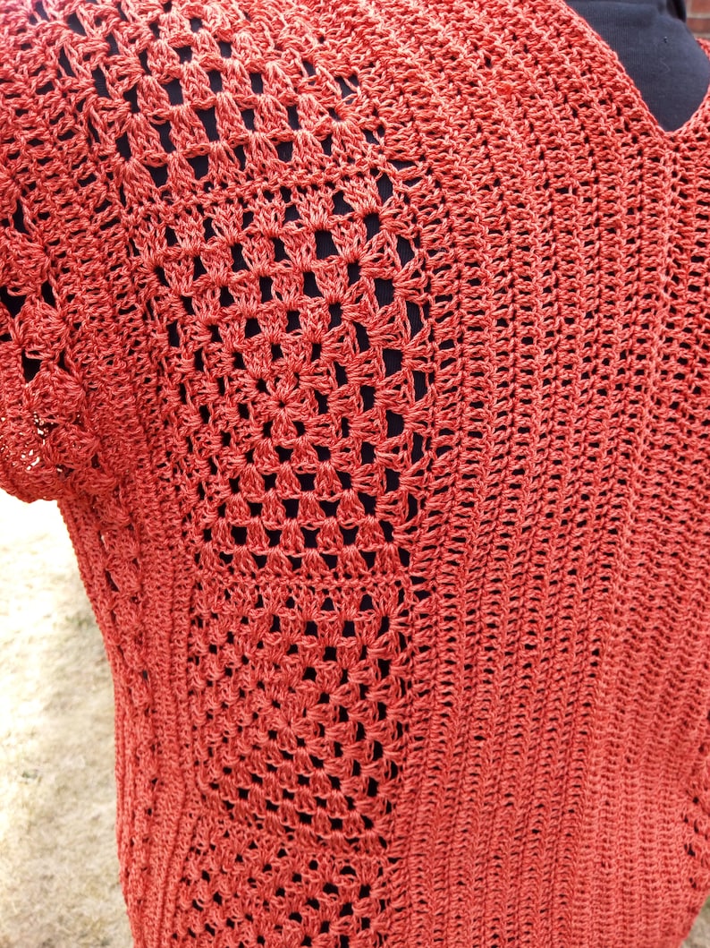 Może przedstawiać: Zbliżenie na dzianinowy top z fakturowanym wzorem o otwartych oczkach. Top jest w żywym pomarańczowym kolorze.