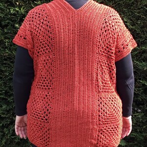 Może przedstawiać: Kr&oacute;tki top na szydełku z dekoltem w kształcie litery V i kr&oacute;tkimi rękawami. Top wykonany jest z przędzy w kolorze rdzy i ma koronkowy wz&oacute;r.