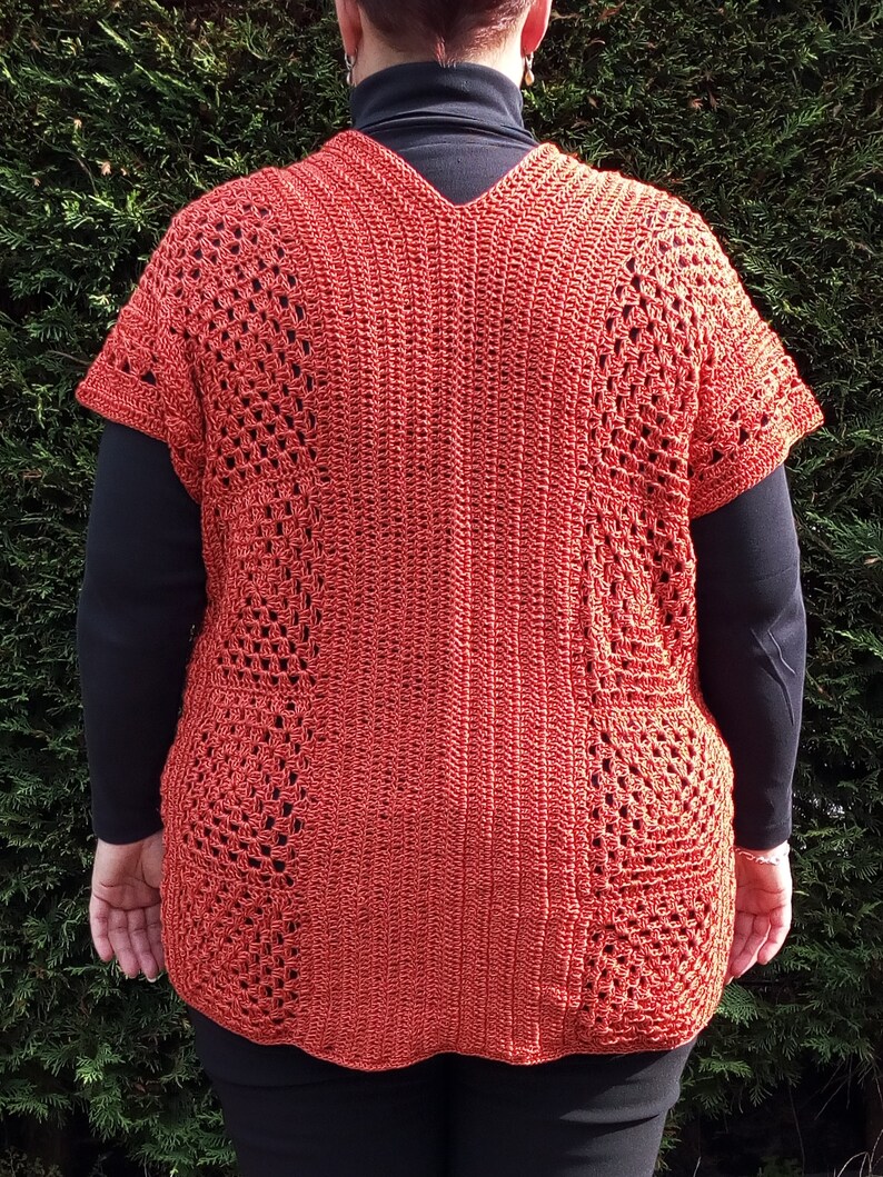 Może przedstawiać: Kr&oacute;tki top na szydełku z dekoltem w kształcie litery V i kr&oacute;tkimi rękawami. Top wykonany jest z przędzy w kolorze rdzy i ma koronkowy wz&oacute;r.