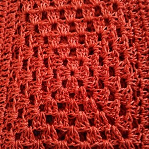 Może przedstawiać: Zbliżenie na czerwoną tkaninę wykonaną na szydełku z powtarzającym się wzorem kwadrat&oacute;w i romb&oacute;w.