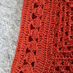 Może przedstawiać: Zbliżenie na tkaninę wykonaną na szydełku z powtarzającym się wzorem otwartych kwadrat&oacute;w. Tkanina jest w żywym pomarańczowym kolorze.