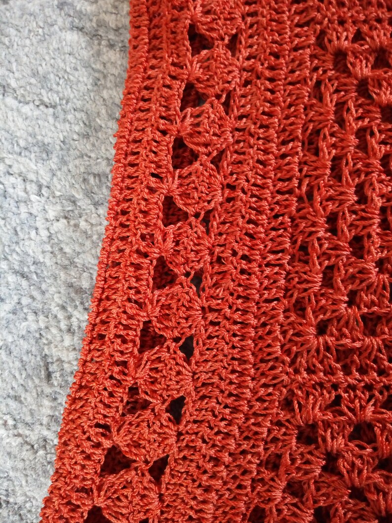 Może przedstawiać: Zbliżenie na tkaninę wykonaną na szydełku z powtarzającym się wzorem otwartych kwadrat&oacute;w. Tkanina jest w żywym pomarańczowym kolorze.