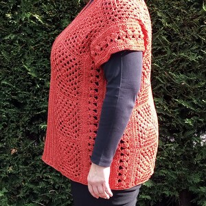 Może przedstawiać: Kr&oacute;tki, luźny top wykonany na szydełku. Top ma ażurowy wz&oacute;r i jest w kolorze jasnopomarańczowym.