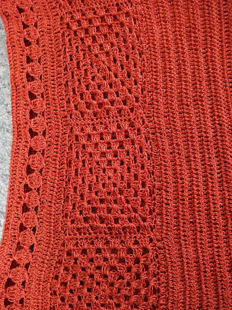 Może przedstawiać: Zbliżenie na tkaninę wykonaną na szydełku z fakturowanym wzorem. Tkanina jest ciemno pomarańczowa i ma powtarzający się wz&oacute;r kwadrat&oacute;w i k&oacute;ł.