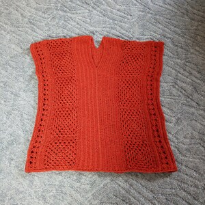 Może przedstawiać: Kr&oacute;tki sweterek wykonany na szydełku w kolorze rdzawo-pomarańczowym z dekoltem w kształcie litery V i ażurowym wzorem.