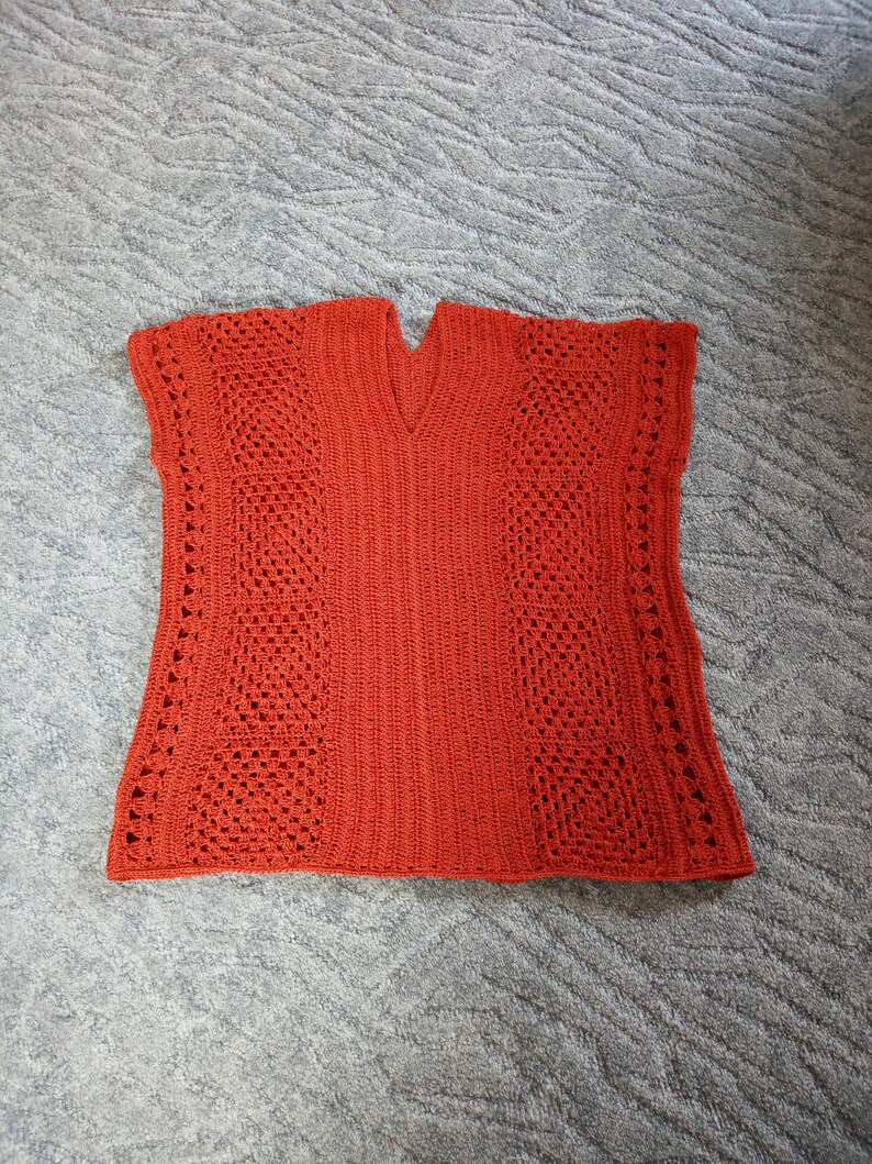 Może przedstawiać: Kr&oacute;tki sweterek wykonany na szydełku w kolorze rdzawo-pomarańczowym z dekoltem w kształcie litery V i ażurowym wzorem.