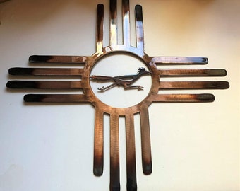 May include: A copper-colored metal wall art piece depicting the symbol of the state of New Mexico, a stylized sun with a roadrunner in the center.