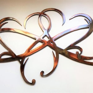May include: A metal wall art piece featuring an abstract design of intertwined infinity symbols and heart shapes. The artwork has a rustic, copper-colored finish with hints of blue and gold, creating a warm, inviting aesthetic.