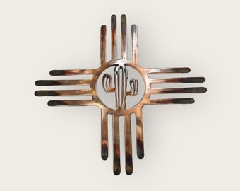 May include: A copper-colored metal cutout of the Zia symbol, a traditional symbol of the Pueblo people of New Mexico, with a cactus design in the center.