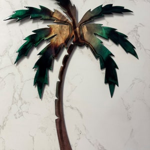 May include: A metal palm tree wall art with a brown trunk and green leaves. The leaves have a textured, metallic finish.