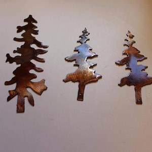 May include: Five metal pine tree wall decor pieces in various sizes. The trees are a rustic brown colour with a metallic finish.