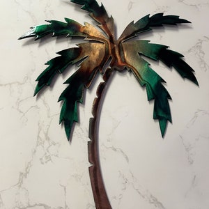 May include: A metal palm tree wall decor with a brown trunk and green leaves. The leaves have a metallic sheen and are textured.