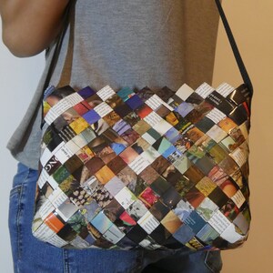 Könnte beinhalten: Eine gewebte Handtasche aus recycelten Magazinseiten. Die Tasche ist braun, schwarz und blau mit einer Vielzahl von Farben und Mustern. Die Tasche hat einen langen Riemen und wird über der Schulter getragen.