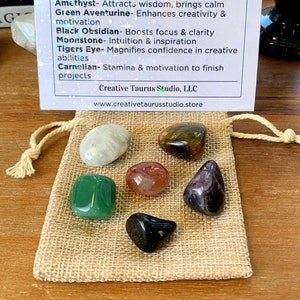 May include: A set of seven tumbled crystals in a small burlap bag. The crystals are amethyst, green aventurine, black obsidian, moonstone, tiger's eye, and carnelian. The bag has a drawstring closure. The crystals are for creativity and inspiration.  CREATIVITY CRYSTAL SET Amethyst- Attracts wisdom, brings calm Green Aventurine- Enhances creativity & motivation Black Obsidian- Boosts focus & clarity Moonstone- Intuition & inspiration Tigers Eye- Magnifies confidence in creative abilities Carnelian-Stamina & motivation to finish projects Creative Taurus Studio, LLC www.creativetaurusstudio.store