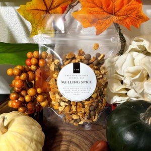 May include: A clear plastic bag filled with dried orange peel and whole spices. The bag has a white label that reads "CREATIVE TAURUS STUDIO, LLC" and "MULLING SPICE". The label also includes instructions for using the spices: "STEEP MULLING SPICES IN CIDER, WINE & MORE TO MAKE A COZY, WINTER DRINK".