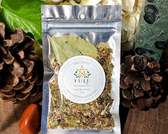 May include: A clear plastic pouch containing a Yule mini simmer pot herb and burn pack, weighing .5 oz. The label features a gold star, green leaves, and text listing ingredients like bay leaf, nutmeg, cinnamon sticks, and juniper berries.
