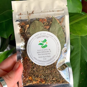 May include: A silver pouch filled with dried herbs and spices labeled "Success & Abundance Mini Simmer Pot Herb/Burn Pack 5 oz" with the website www.creativetaurusstudio.store. The pouch is labeled with a list of ingredients including ginger, bay leaf, rosemary, clove, basil, allspice, nutmeg, meadowsweet, cinnamon, orange peel, peppermint, and dandelion leaf.