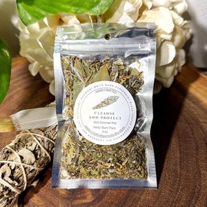 May include: A small clear plastic bag filled with dried herbs and spices. The bag has a white label with the text "CLEANSE AND PROTECT" and "Mini Simmer Pot Herb/Burn Pack 5 oz www.creativetaurusstudio.store".