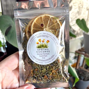 May include: A clear, sealed bag containing a Spring Cleanse simmer pot herb scent pack. The label reads "Spring Cleanse" and "Simmer Pot Herb Scent Pack." The bag contains dried herbs, citrus slices, and the text "Hand Crafted." The bag weighs 5 oz.
