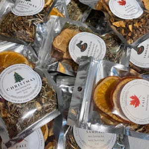 May include: Assortment of small, clear, resealable bags filled with dried herbs and fruit slices. The bags are labeled with the names "Christmas", "Samhain", and "Fall". Each bag contains a mini simmer pot herb/burn pack, 5 oz.