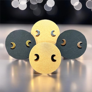 May include: Three display cards with crescent moon earrings. The cards are black, gold, and white. The earrings are silver, gold, and black.