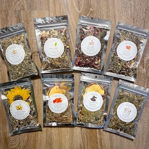 Puede incluir: Surtido de mezclas de té de hierbas en bolsas transparentes y resellables. Cada bolsa presenta una etiqueta redonda con texto e ilustraciones botánicas. Las mezclas incluyen flores secas, hierbas y frutas. Las etiquetas incluyen los nombres Imbolc, Beltane, Ostara, Litha, Lammas, Mabon, Samhain y Yule.