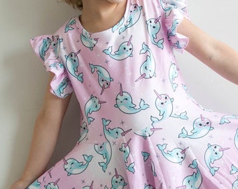 May include: A pink and white dress with a narwhal print. The dress has a ruffled neckline and short sleeves.