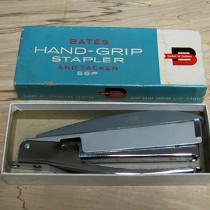 Puede incluir: Una grapadora y grapadora manual Bates Hand-Grip 56P plateada en su caja original. La caja es azul y blanca con el logotipo de Bates y el texto "Toma todas las grapas estándar" y "También grapas Bates más largas 3/16"".