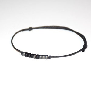 May include: A black cord bracelet with a row of small, dark grey and black beads.