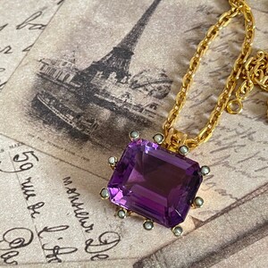 May include: A gold chain necklace with a large, rectangular, faceted amethyst pendant. The pendant is set in a gold frame with small pearl accents.