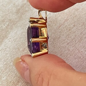 May include: A gold pendant featuring a large, faceted amethyst gemstone surrounded by smaller, clear gemstones. The pendant has a bail for attaching to a chain.
